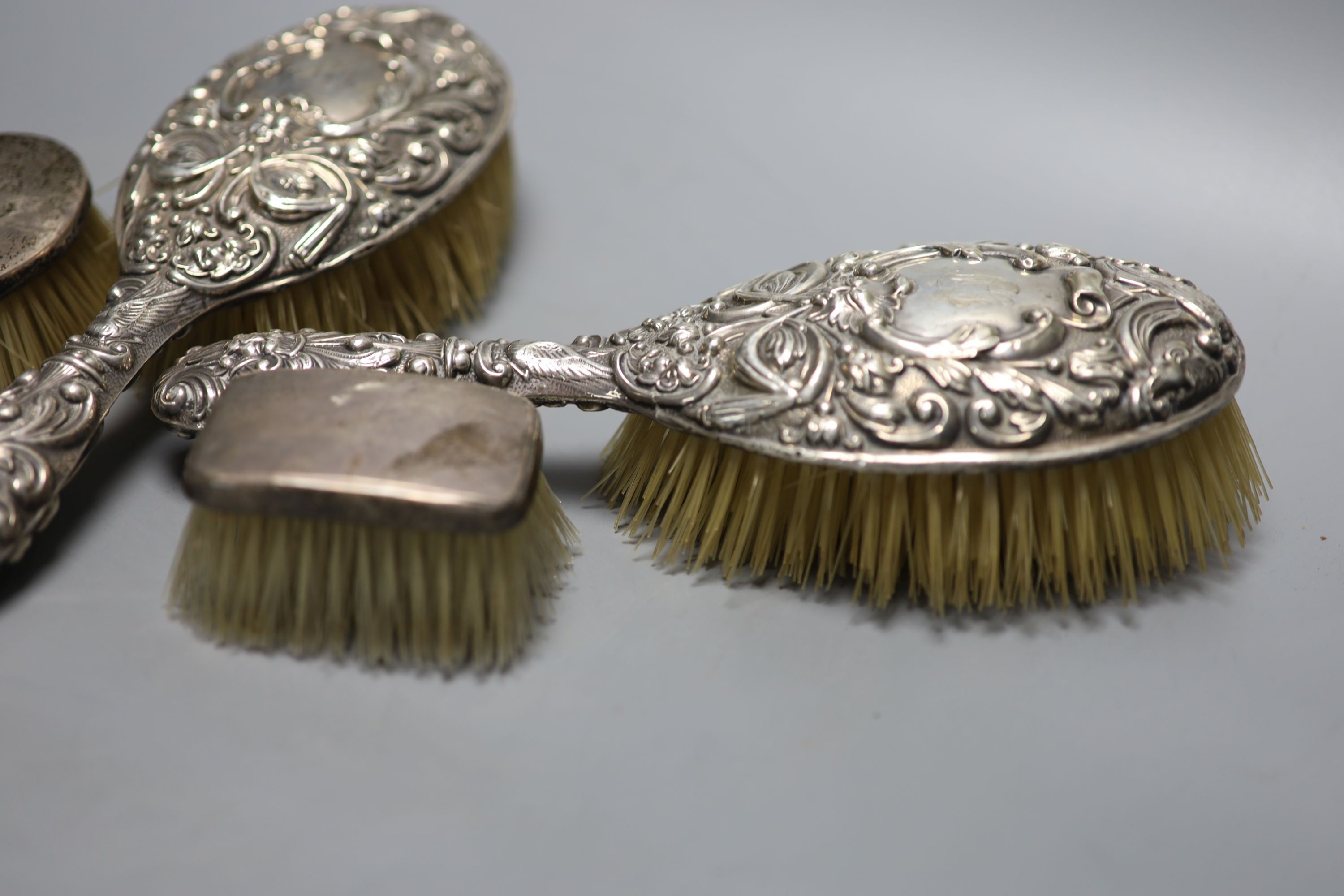 A pair of Edwardian repousse silver backed hair brushes and two other brushes.